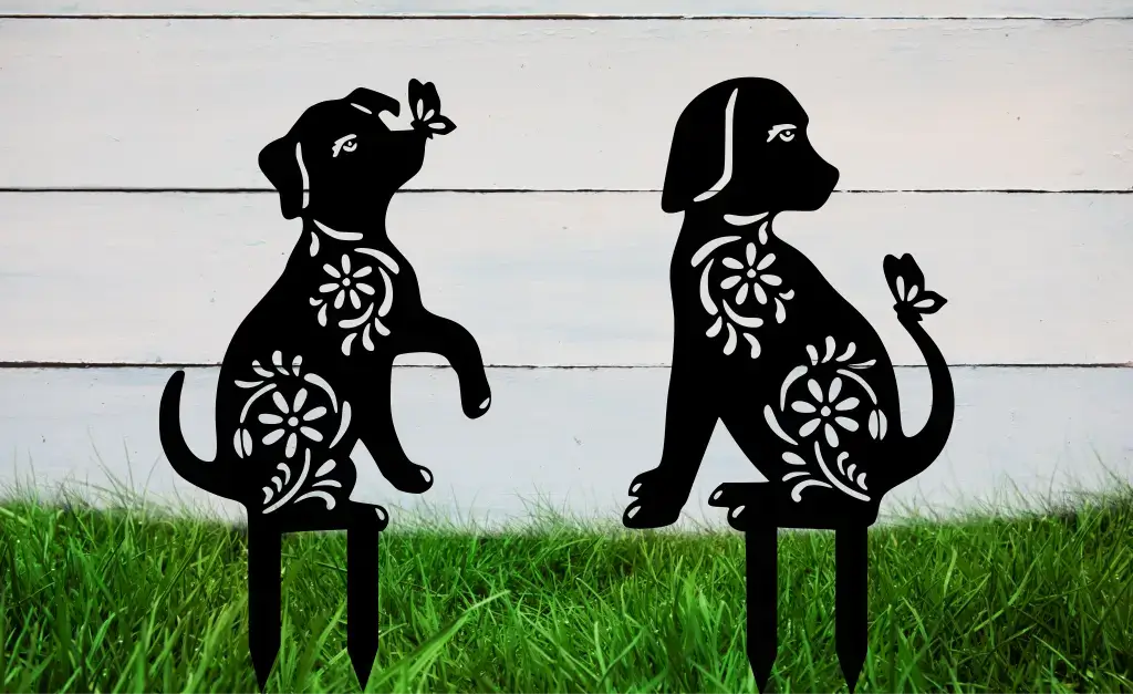 Two black floral-patterned dog-shaped metal garden stakes placed against a white wooden background.
