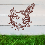 Delicate metal wall art featuring a hummingbird with intricately detailed wings and tail, surrounded by swirling vine patterns, finished in Manor Red powder coating, mounted on a rustic white wooden backdrop, perfect for adding a touch of nature to an outdoor space.