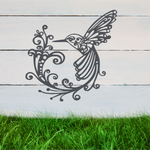 Delicate metal wall art featuring a hummingbird with intricately detailed wings and tail, surrounded by swirling vine patterns, finished in Berry Grey Gloss powder coating, mounted on a rustic white wooden backdrop, perfect for adding a touch of nature to an outdoor space.