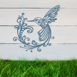 Delicate metal wall art featuring a hummingbird with intricately detailed wings and tail, surrounded by swirling vine patterns, finished in Wedgwood Satin powder coating, mounted on a rustic white wooden backdrop, perfect for adding a touch of nature to an outdoor space