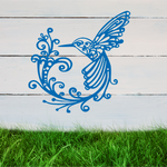 Delicate metal wall art featuring a hummingbird with intricately detailed wings and tail, surrounded by swirling vine patterns, finished in Blaze Blue Gloss powder coating, mounted on a rustic white wooden backdrop, perfect for adding a touch of nature to an outdoor space.
