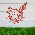 Delicate metal wall art featuring a hummingbird with intricately detailed wings and tail, surrounded by swirling vine patterns, finished in Signal Red powder coating, mounted on a rustic white wooden backdrop, perfect for adding a touch of nature to an outdoor space.